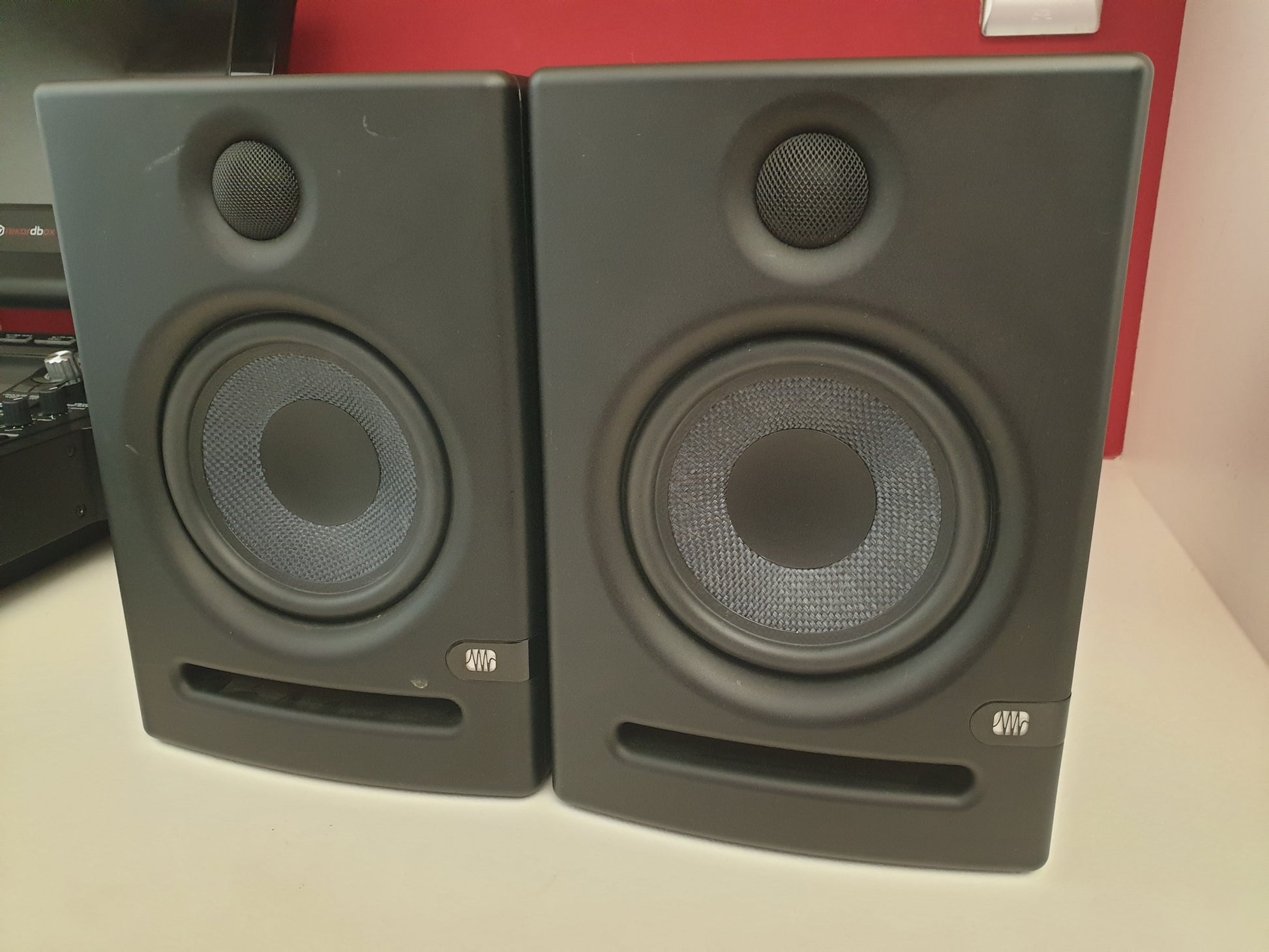 Pair of gray studio monitors on a surface with a red background